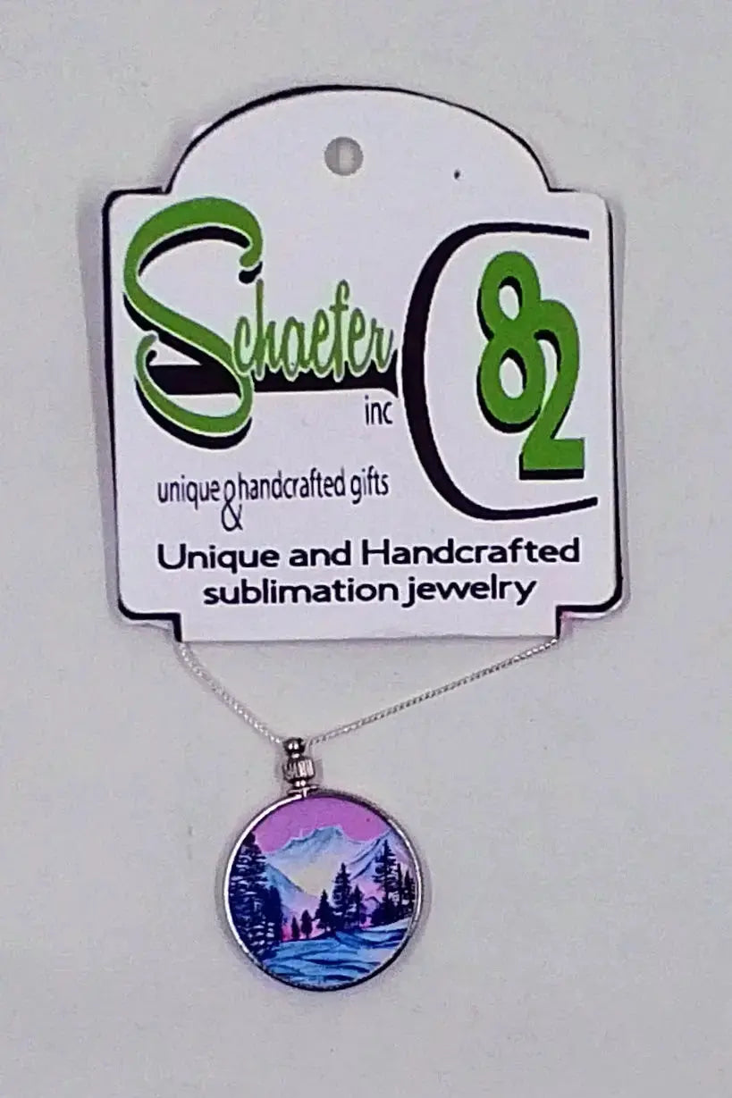 Mountain necklace with an image of pink skies and purple mountains and trees in the forefront and are sandwiched between two pieces of glass for protection.