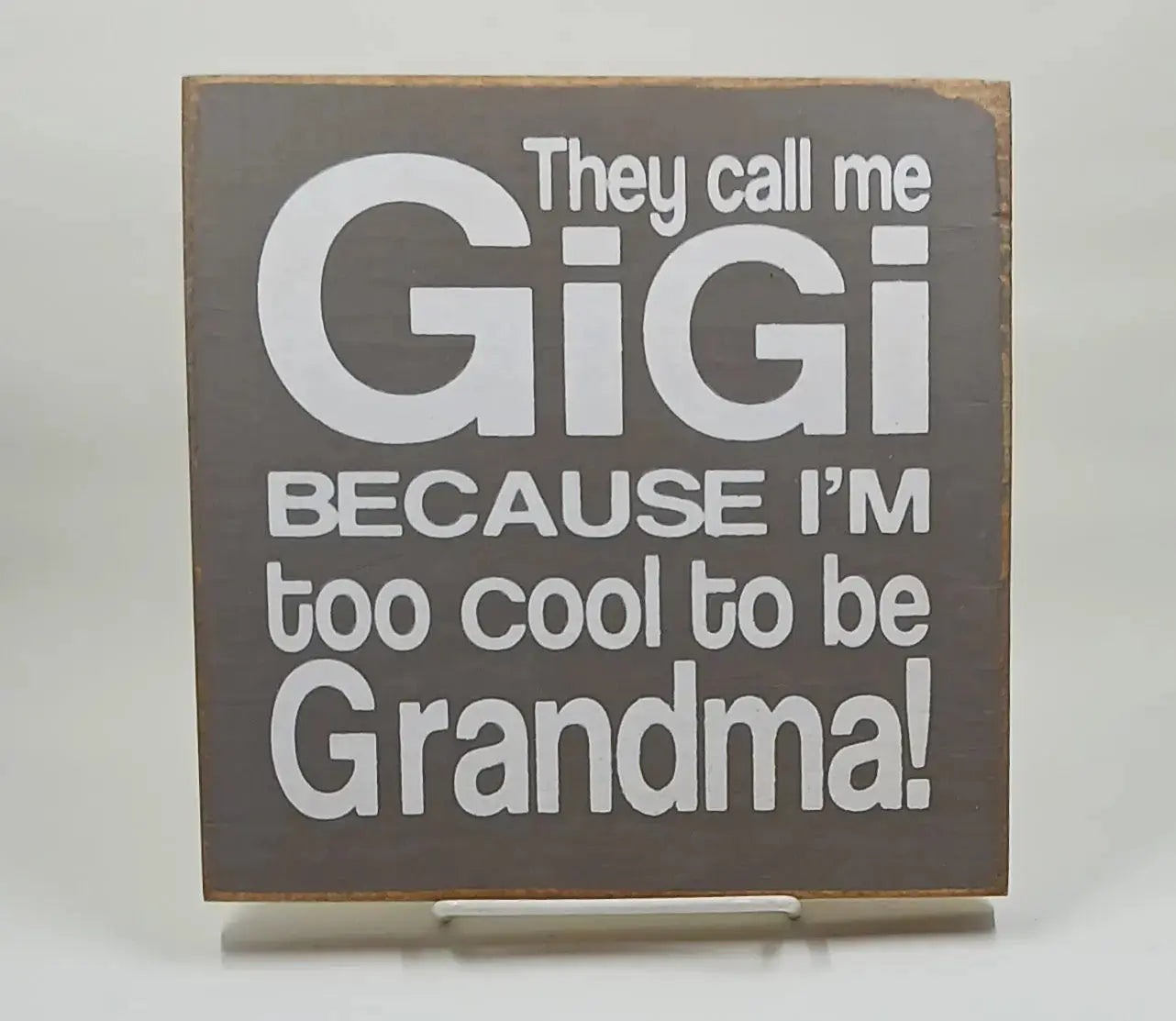 A 7 inch by 7 inch brown wooden sign with white lettering saying "they call me gigi because im too cool to be grandma