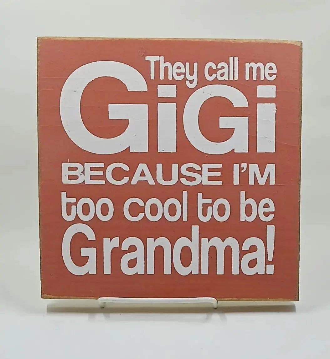 7 inch by 7 inch orange wooden sign that says "they call me gigi because im too cool to be grandma" in white lettering.