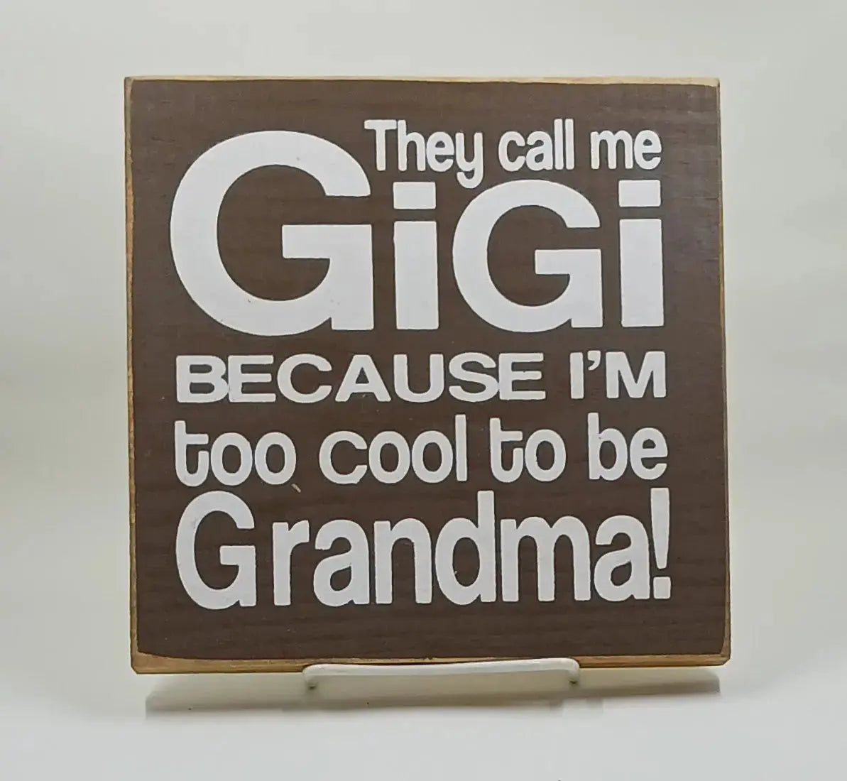 7 inch by 7 inch wooden sign that is painted brown and with white lettering says "They call me Gigi because Im too cool to be grandma".