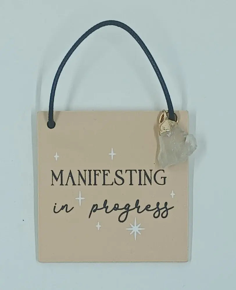 This metaphysical gift is a miniature wooden sign that says "manifesting in progress"