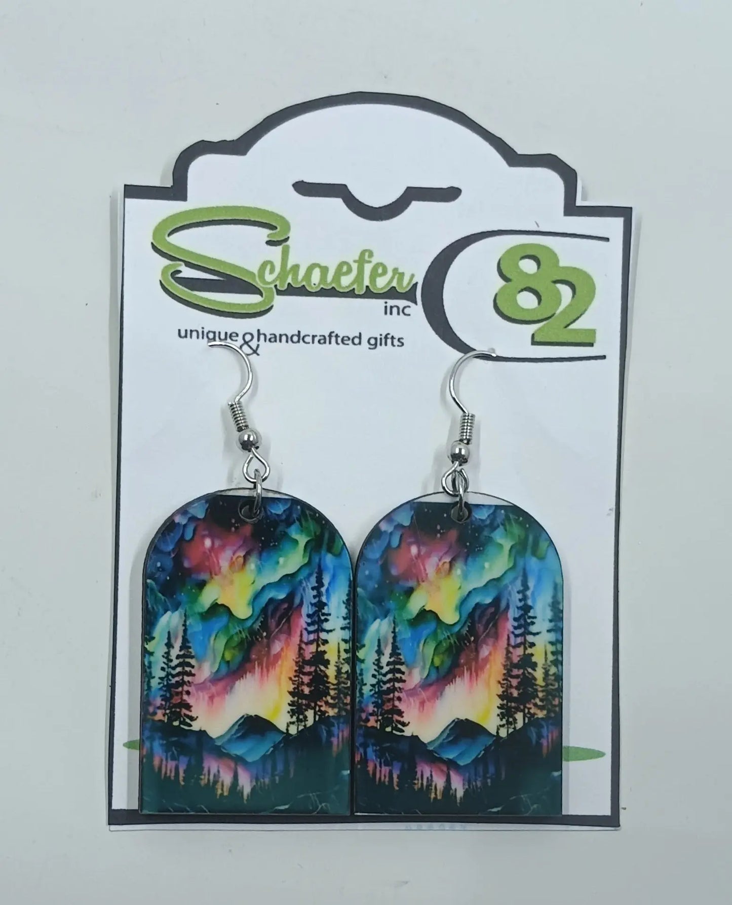 These handcrafted earrings are covered in the vibrant and colorful rainbow colors of the northern lights with mountains and trees silhouetted in the forefront. 