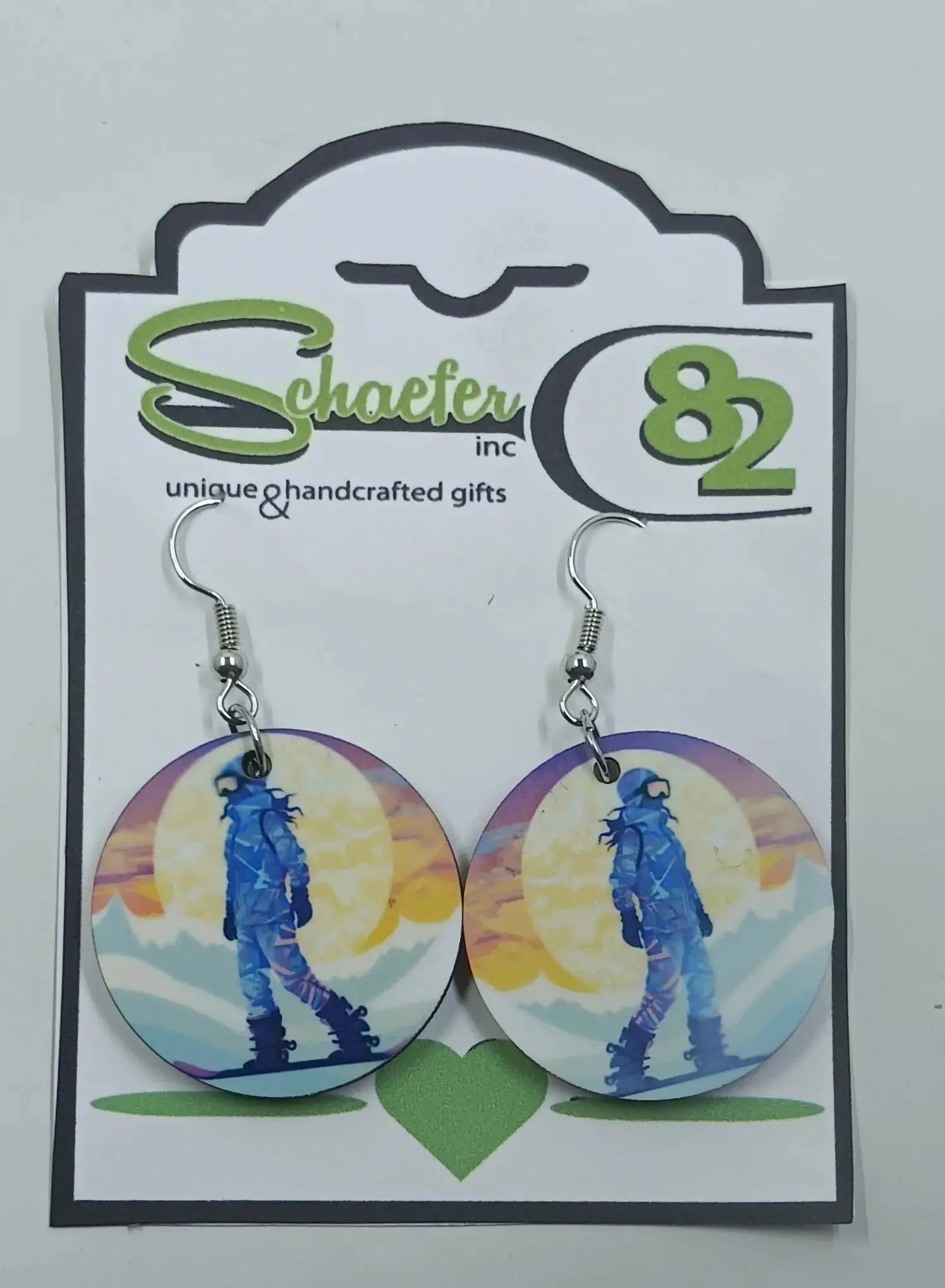 These gorgeous snowboarding earrings are made using sublimation  techniques. there is a snowboarder, in front of a huge sun, and is snowboarding down the mountain
